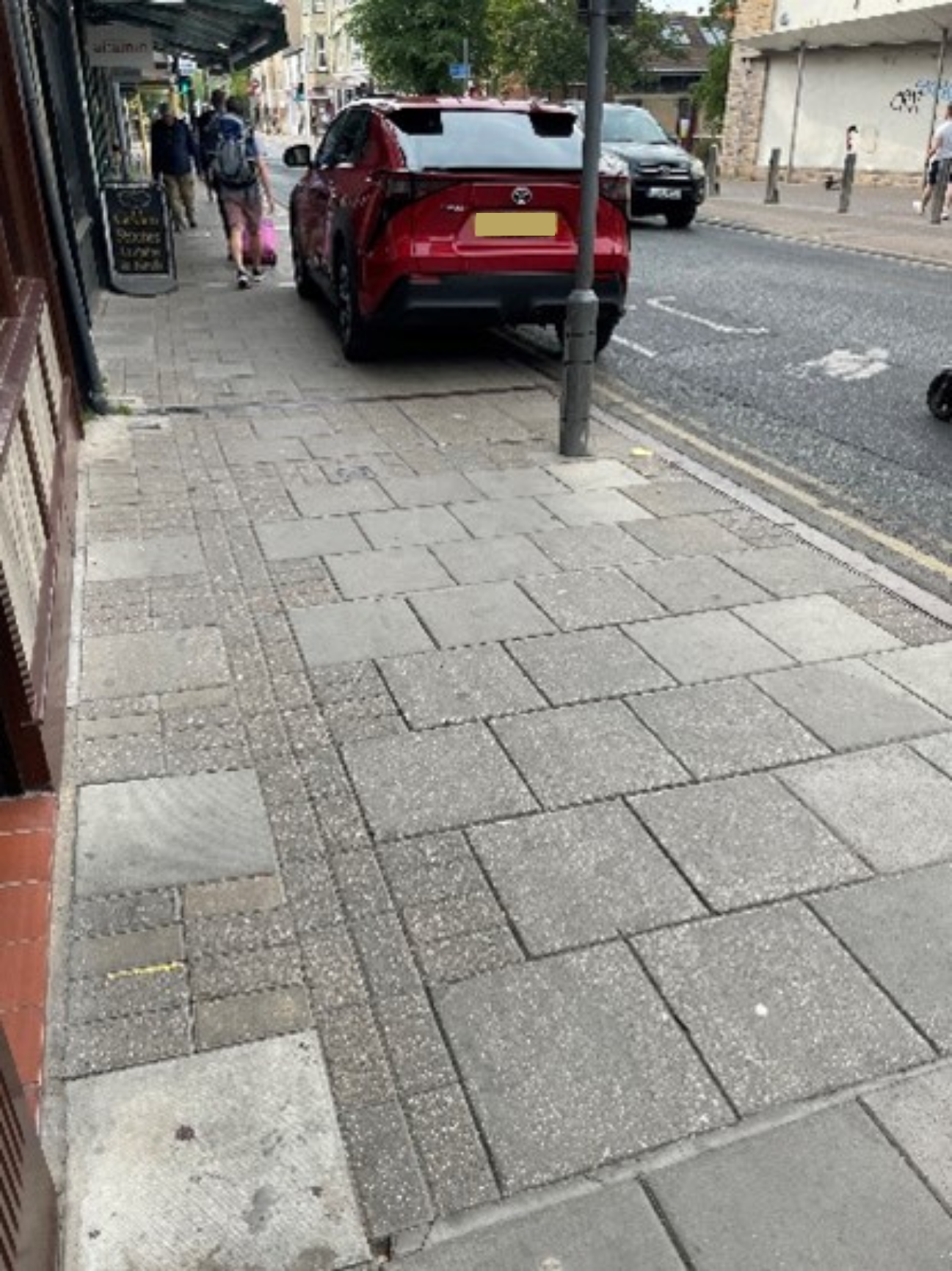 A parked car partially blocking a pavement