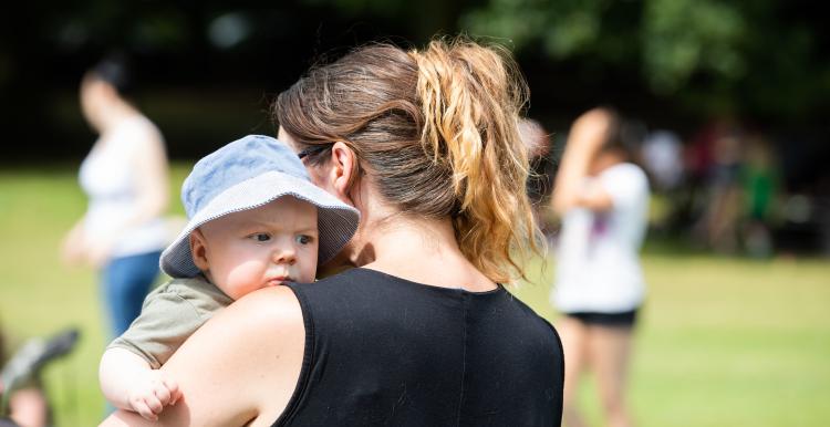 A mother holding a baby. She is standing in park.