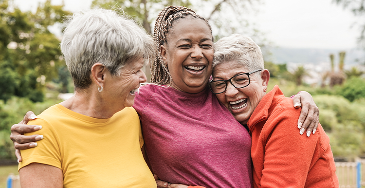 Three women outdoors, laughing and hugging