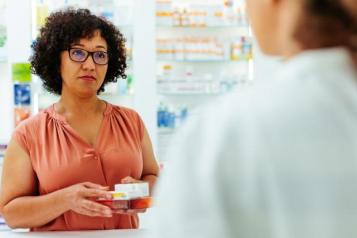 a photo of a woman in a pharmacy, holding medication in her hand