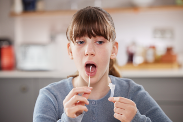 Picture shows teenage girl swabbing the back of her throat as part of a lateral flow test 