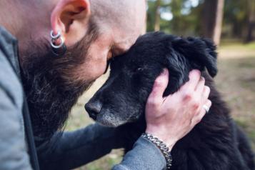 Sideways view of man holding an old dog and looking sad 