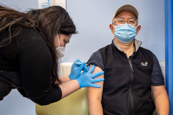 Man indoors wearing face covering receiving a Covid-19 vaccination from a health worker