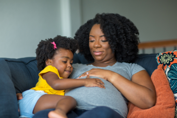 Pregnant woman and young daughter sitting on couch