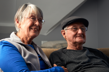 Picture shows older couple sat on sofa at home 