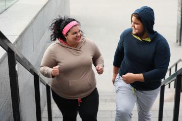 A woman and a man out jogging. They are climbing a flight of concrete steps and smiling at each other.