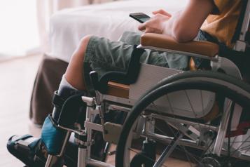 A young wheelchair user in a bedroom and holding a mobile phone