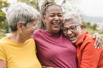 Three older women outdoors hug and smile 