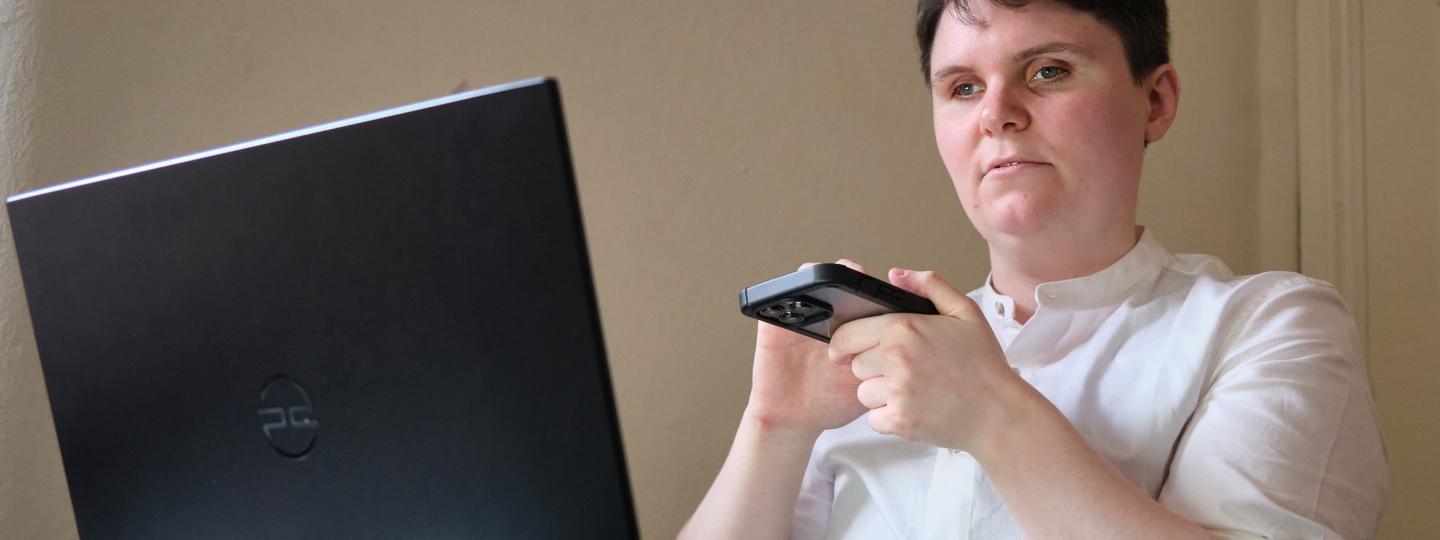 A visually impaired man sat at a desk with a laptop in front of them. The person is using a screen reader.