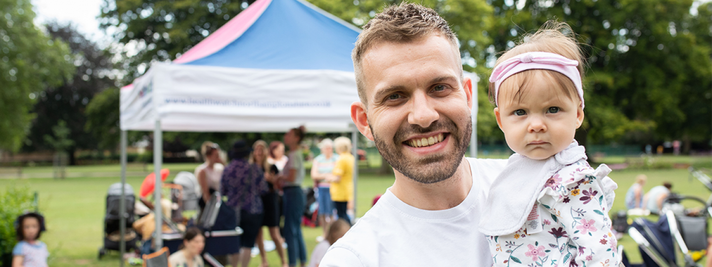 Picture shows man holding toddler at an outdoor children's event