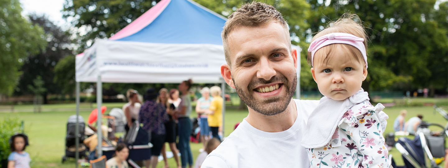 Picture shows man holding toddler at an outdoor children's event 